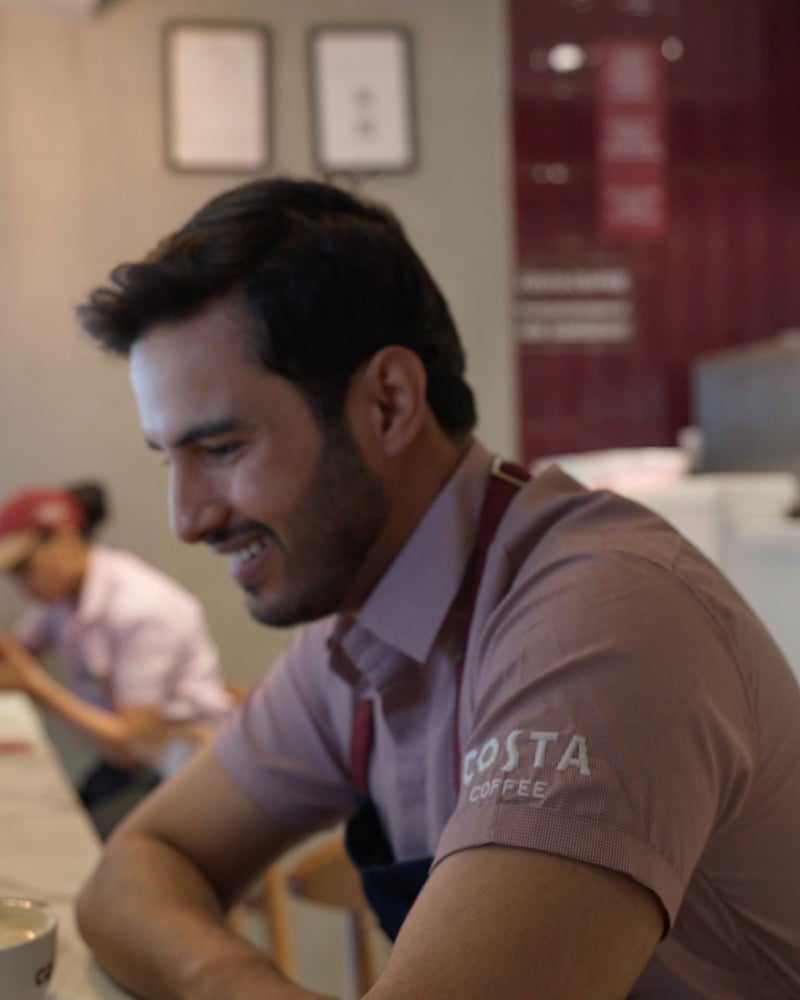 Smiling barista at a Costa Coffee counter